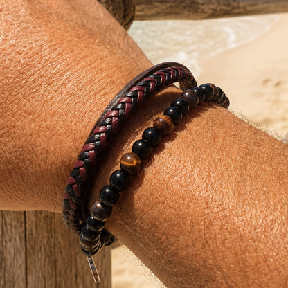 Zwart-rode vegan leren herenarmband met kralen om een mannenpols op het strand.