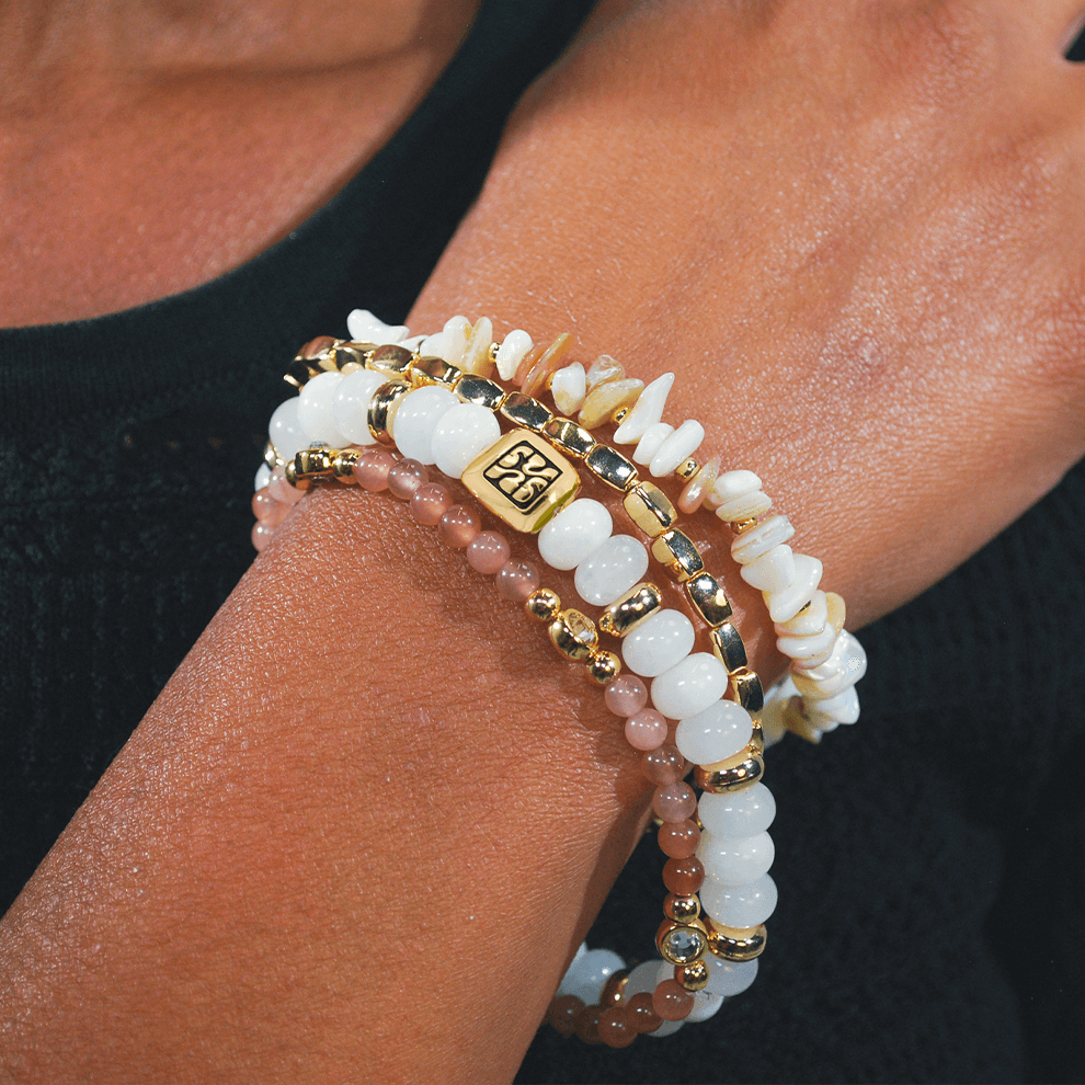 Close-up van de Blush armbandenset van SummerGear, gedragen om de pols met witte en zachtroze kralen, schelpdetails en goudkleurige accenten.