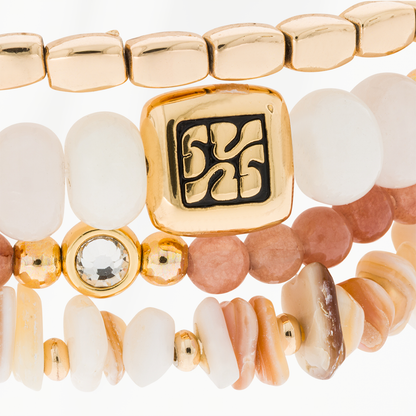 Close-up van de Blush armbandenset van SummerGear met witte ovale kralen, roze natuurstenen kralen, schelpdetails en een goudkleurig ornament.