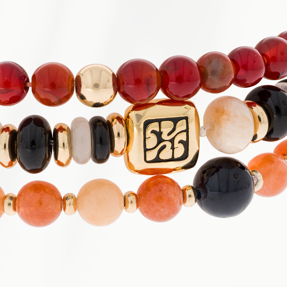 Close-up van de Sunset Mix armbandenset van SummerGear met dieprode, oranje en zwarte kralen, platte naturel kralen en een goudkleurig ornament.
