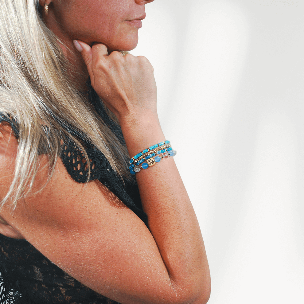 Blue Coast armbandenset van SummerGear gedragen om de pols, met blauwe en turquoise kralen en goudkleurige details bij een zwarte kanten top.