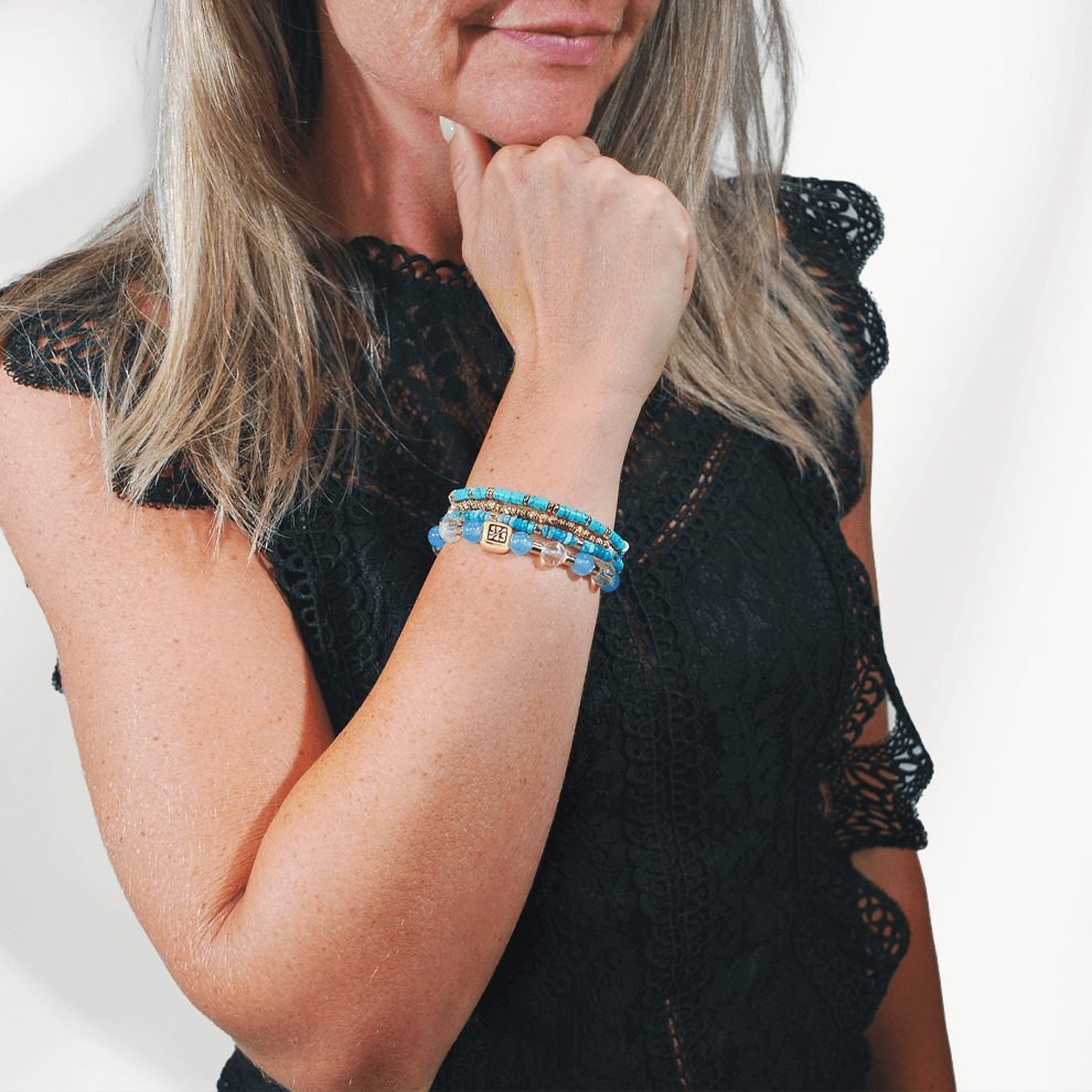 Model draagt de Blue Coast armbandenset van SummerGear met blauwe en turquoise kralen en goudkleurige details bij een zwarte top.