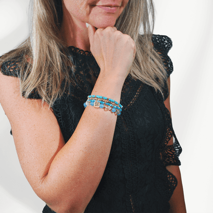 Model draagt de Blue Coast armbandenset van SummerGear met blauwe en turquoise kralen en goudkleurige details bij een zwarte top.