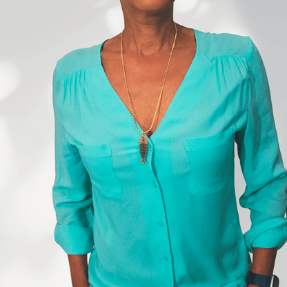 Model draagt de lange goudvergulde damesketting Fish van SummerGear met blauwgroene vishanger bij een turquoise blouse