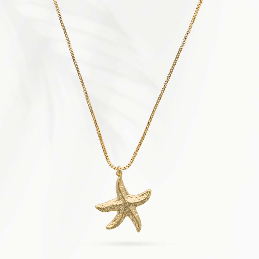 Model draagt de goudvergulde damesketting Star van SummerGear met zeesterhanger bij een blauw-wit gestreepte blouse.
