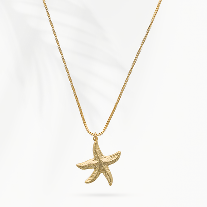 Model draagt de goudvergulde damesketting Star van SummerGear met zeesterhanger bij een blauw-wit gestreepte blouse.