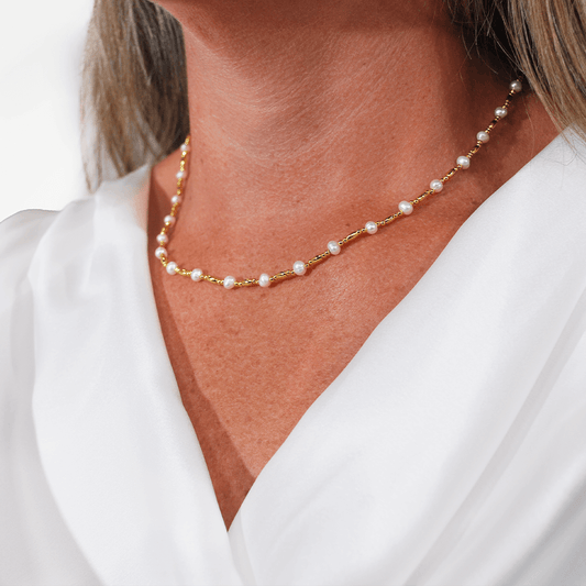 Model draagt de Ripple Chain parelketting van SummerGear met kleine witte parels en fijne goudvergulde schakels, gecombineerd met een witte blouse.
 Kopiëren