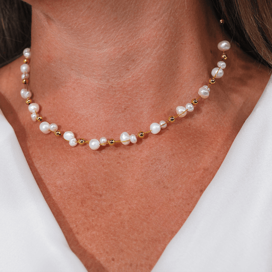 Model draagt de Pure Pearl parelketting van SummerGear met echte witte parels en kleine goudvergulde kralen bij een witte blouse.