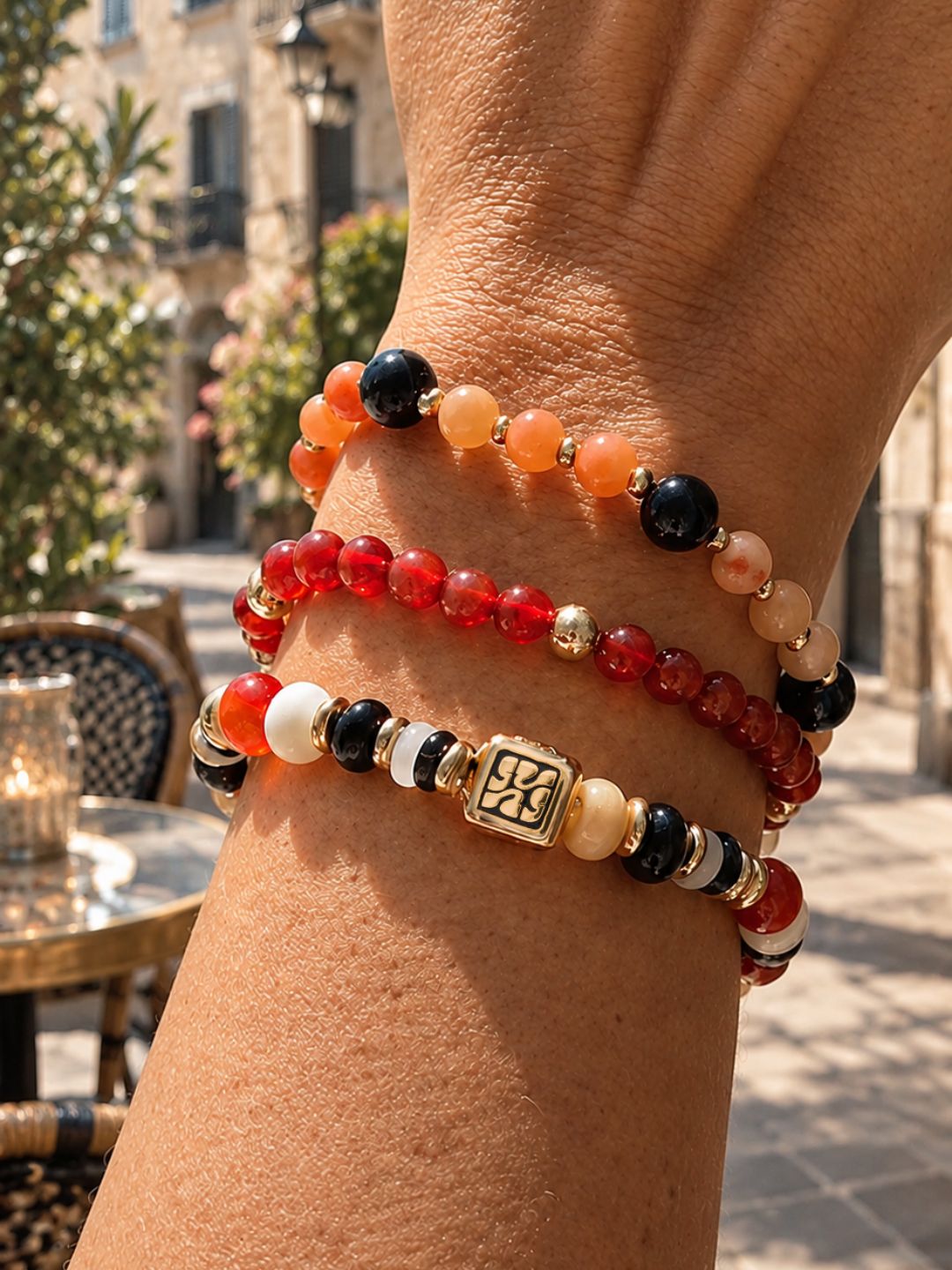Armbandenset Sunset Mix van SummerGear met rode, oranje en zwarte kralen en goudkleurige details, gedragen om de pols.