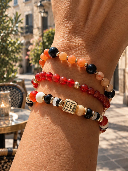 Armbandenset Sunset Mix van SummerGear met rode, oranje en zwarte kralen en goudkleurige details, gedragen om de pols.